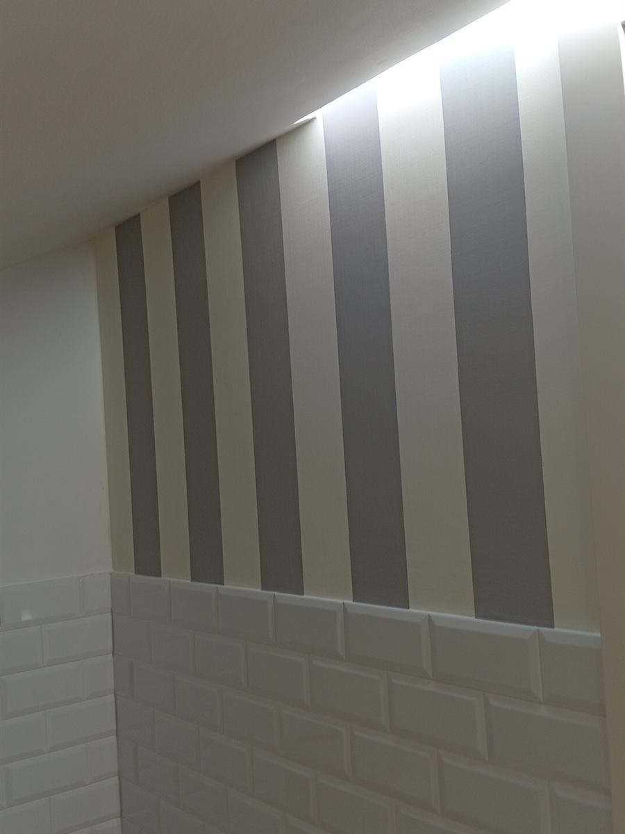 Baño abuhardillado con pared a rayas grises y blancas sobre azulejo