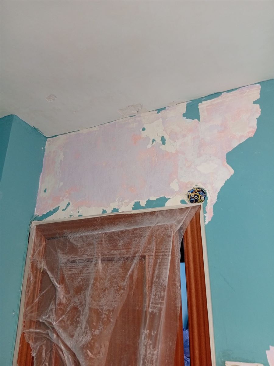 Antes: pared azul con la pintura y el papel levantados alrededor de una puerta